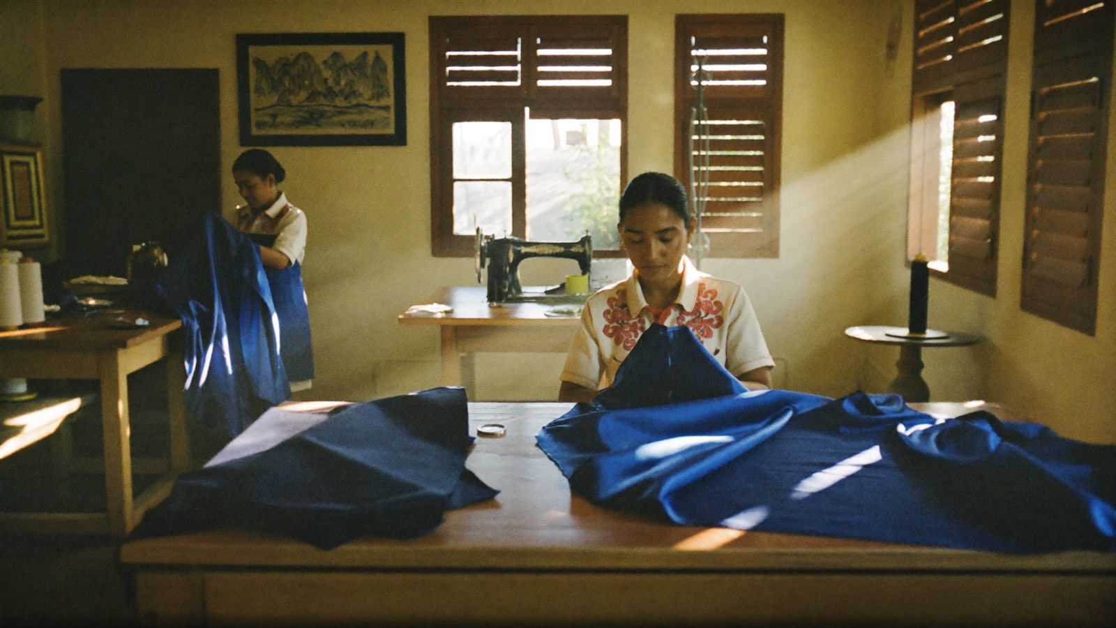 The sunlit Colombo atelier — wooden tables, bolts of jade and cobalt silk, a seamstress at work